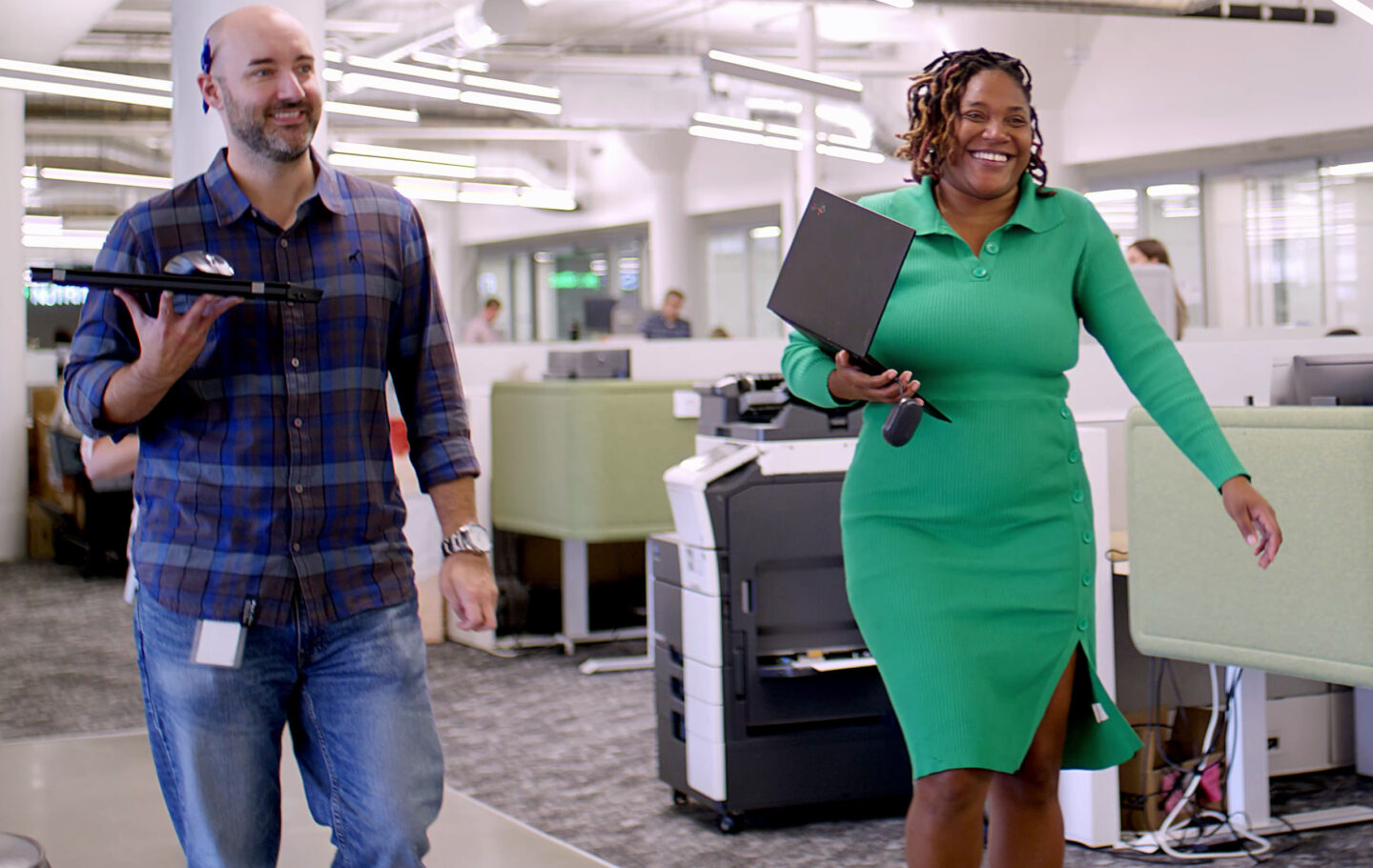 A woman and a man walking into the Premier Nutrition office for a meeting. They are both holding laptops and smiling.