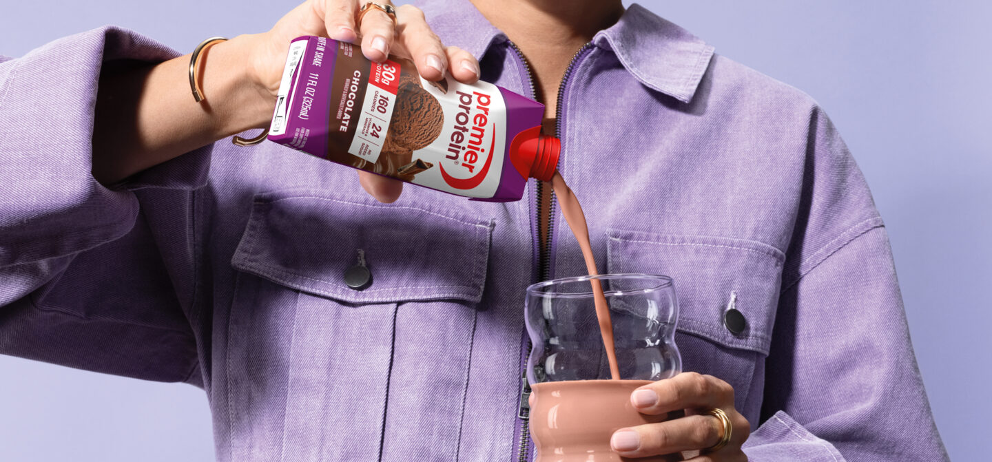 A man pouring a chocolate premier protein shake into a glass.