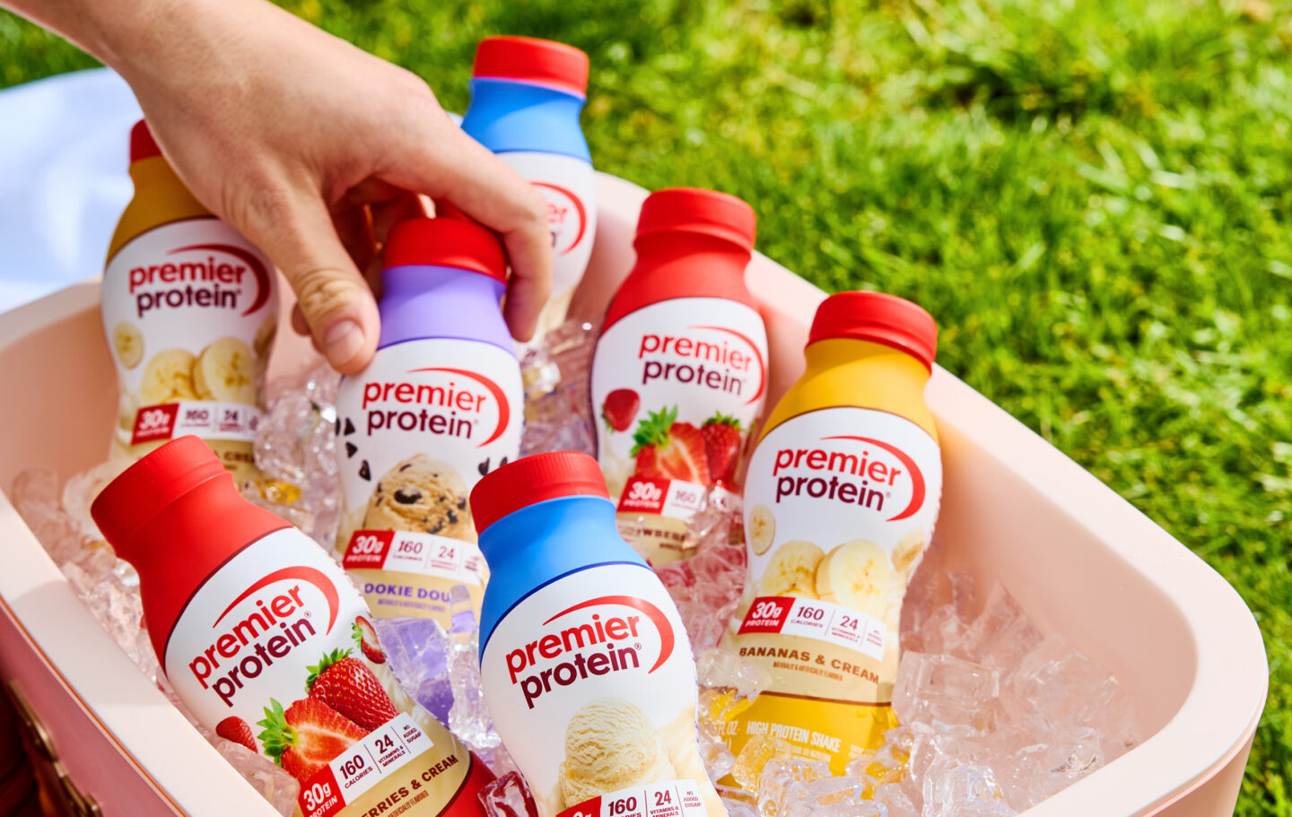 A hand reaching into a cooler filled with ice and Premier Protein Shakes.
